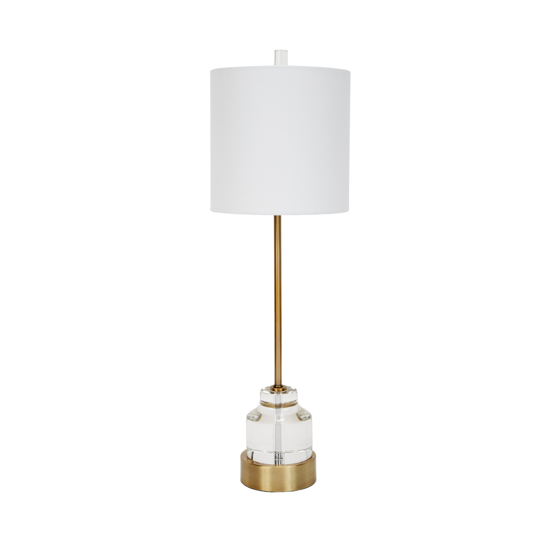 Modern table lamp with white drum shade, gold stem, and clear glass base on white background