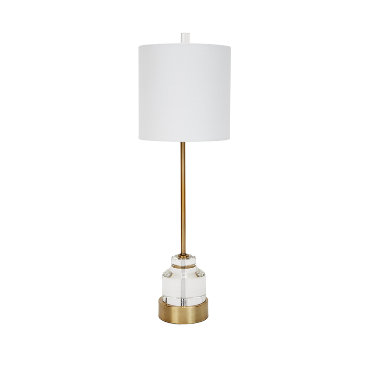 Modern table lamp with white drum shade, gold stem, and clear glass base on white background