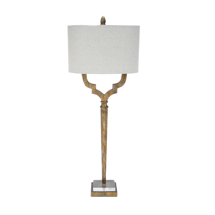Distressed gold metal table lamp with sculpted base and beige drum shade on white background