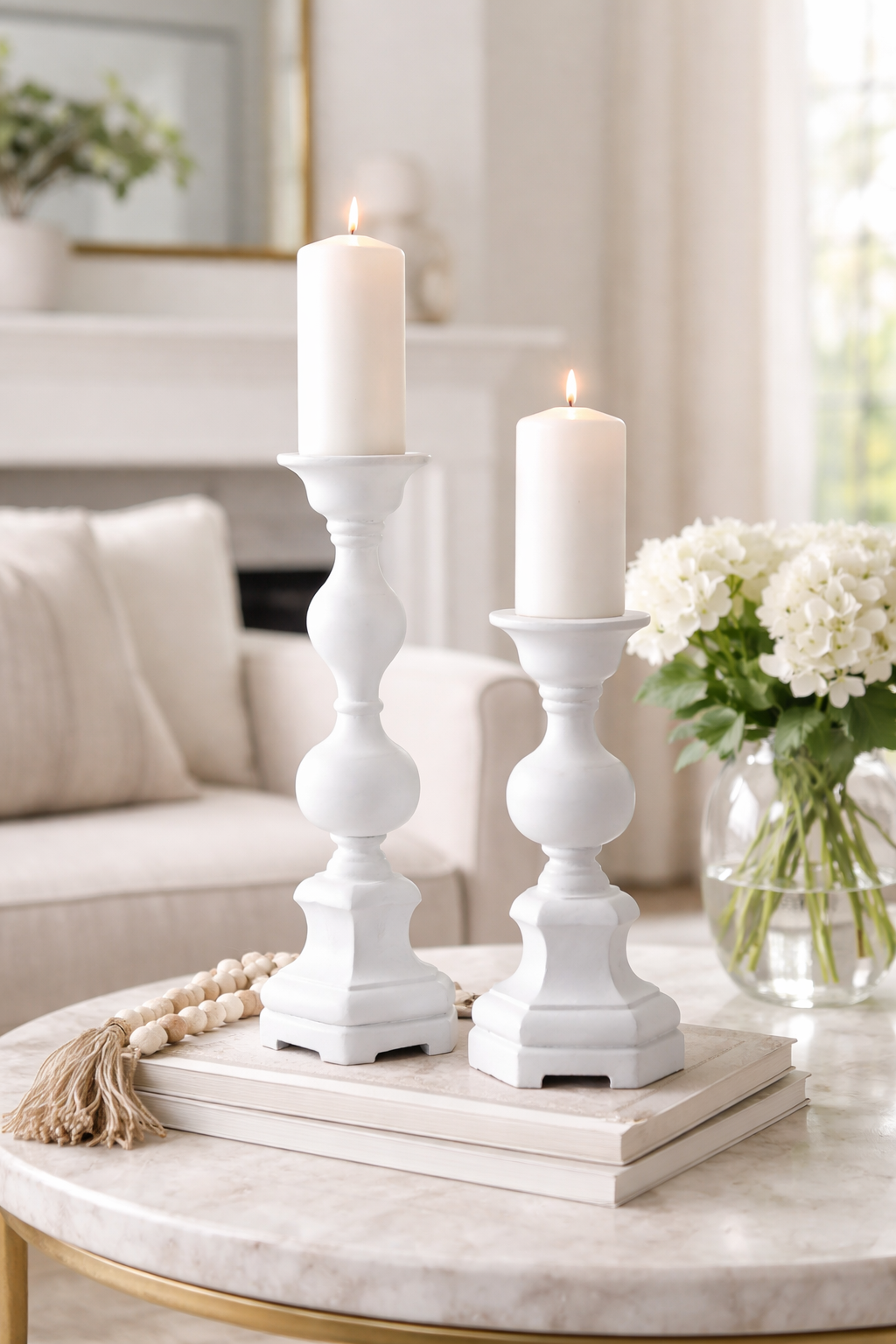 Two white candles in decorative candlesticks on a marble table with a blurred background