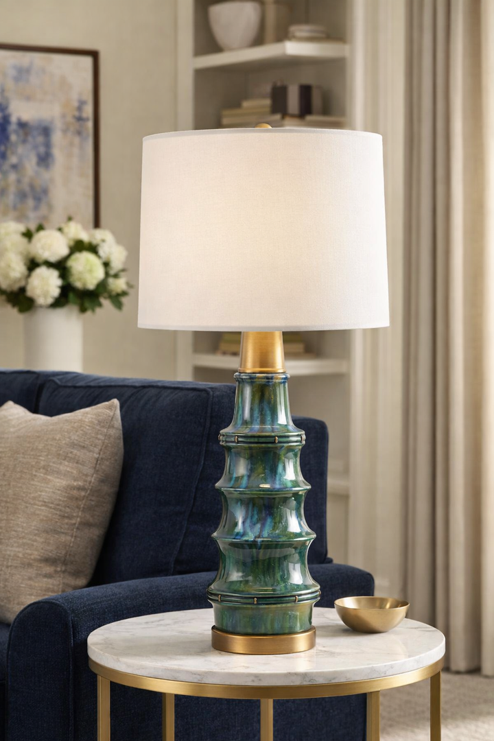 Decorative lamp with a green and gold base on a marble table in a living room setting.