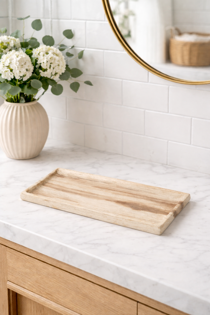 Wooden tray on a white countertop with a vase of flowers and a mirror in the background.