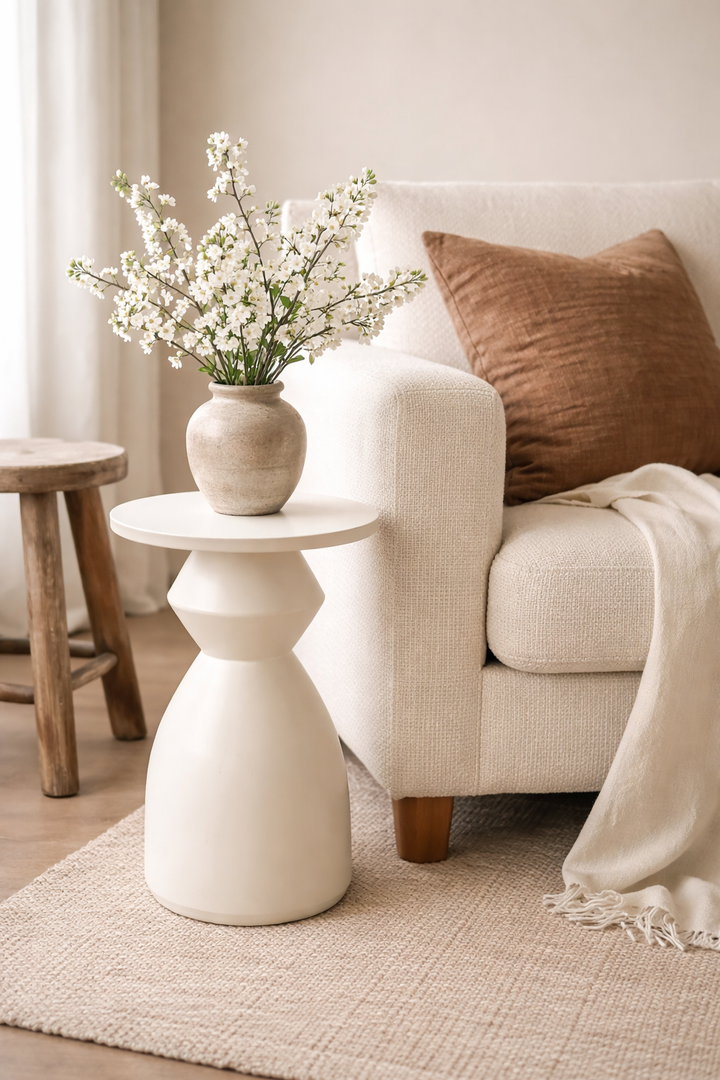 White side table with a vase of flowers next to a beige armchair with a brown pillow.