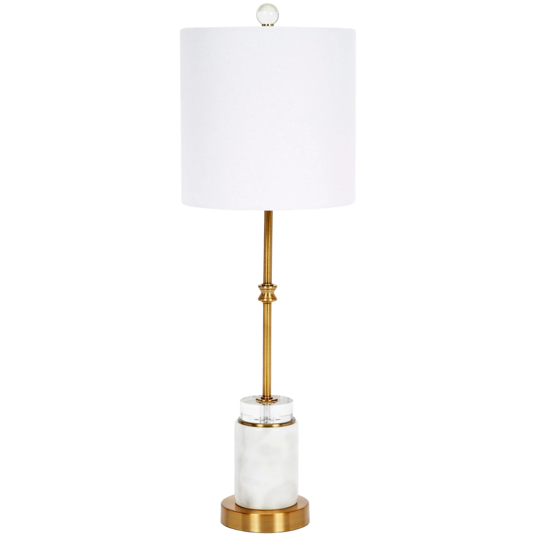 A modern table lamp with a white drum shade, a brushed gold metal stem, a white marble cylindrical base, and a round gold foot ring, shown on a pure white background.