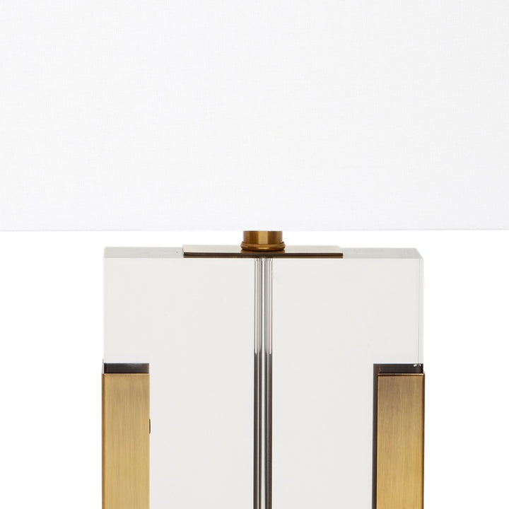 Table lamp with white shade, clear column, and brass accents on the sides