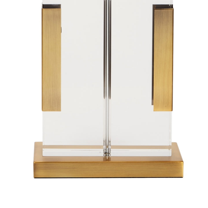 Table lamp with white shade, two brass side panels, clear stem, and brass base