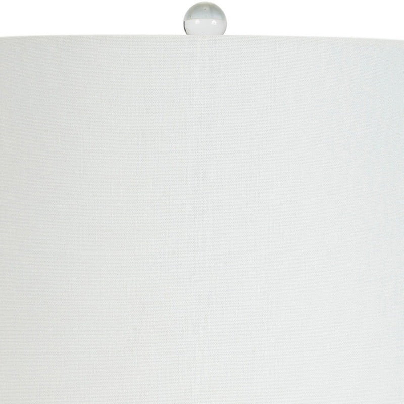 White linen lampshade with gold finial atop white ceramic lamp base
