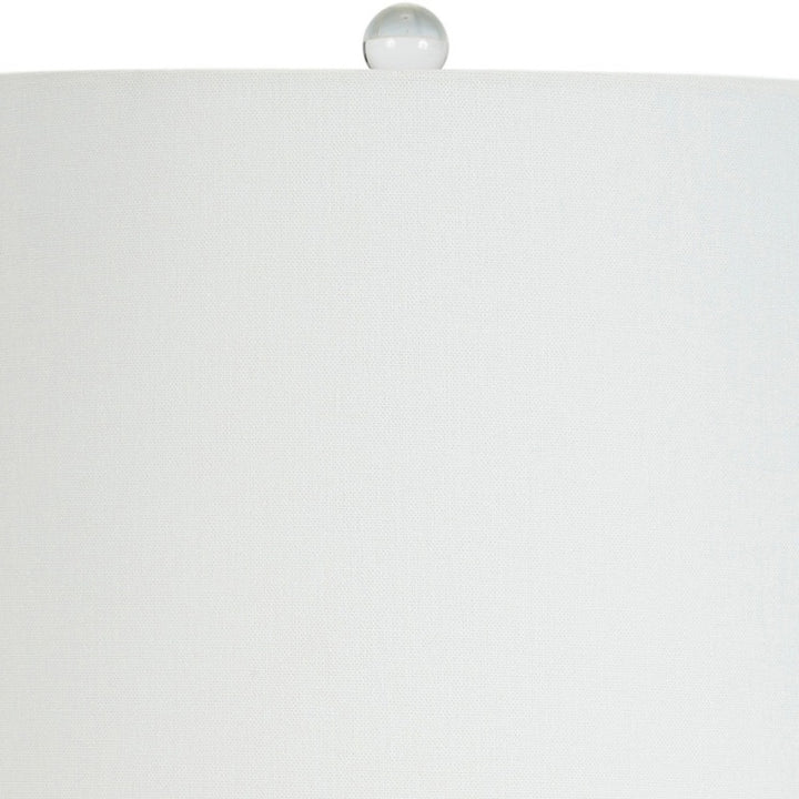White linen lampshade with gold finial atop white ceramic lamp base