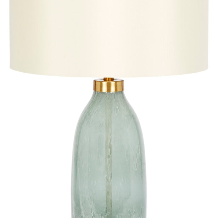 Table lamp featuring off-white drum shade and tall pale green glass bottle base