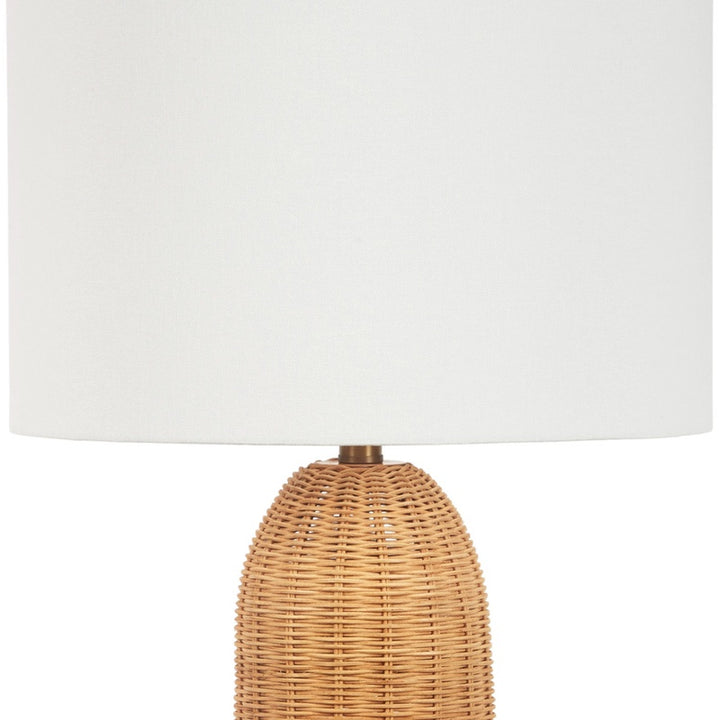 Table lamp with white linen shade and woven rattan base, brass stem visible