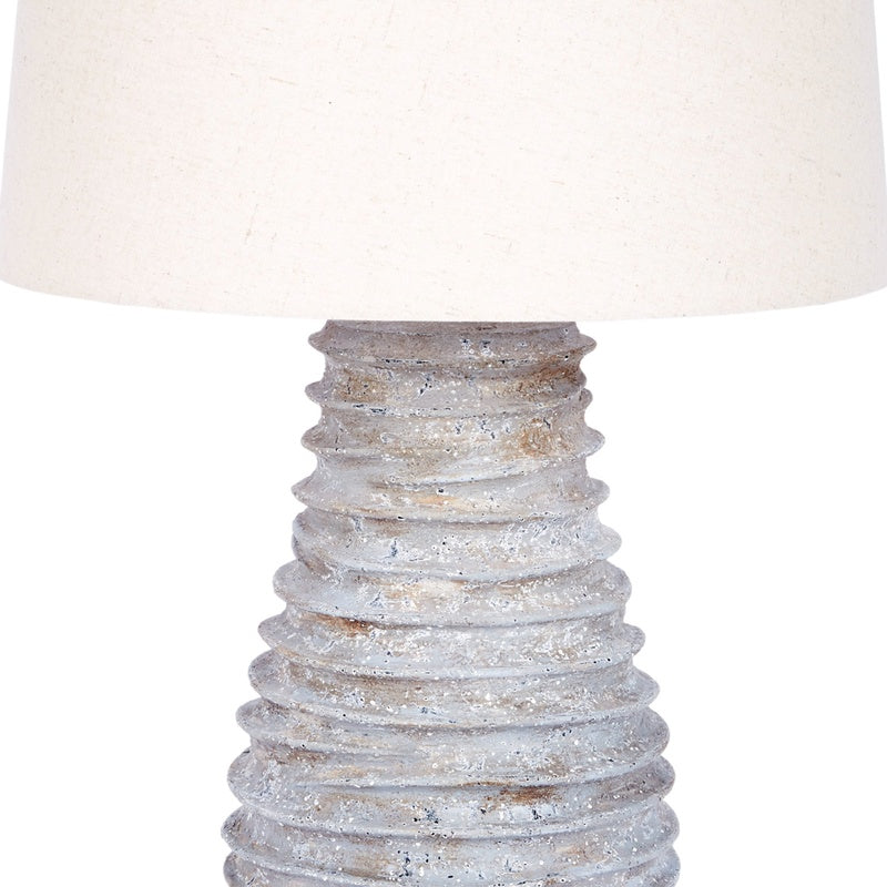 Table lamp with off-white linen shade over distressed silver ribbed base