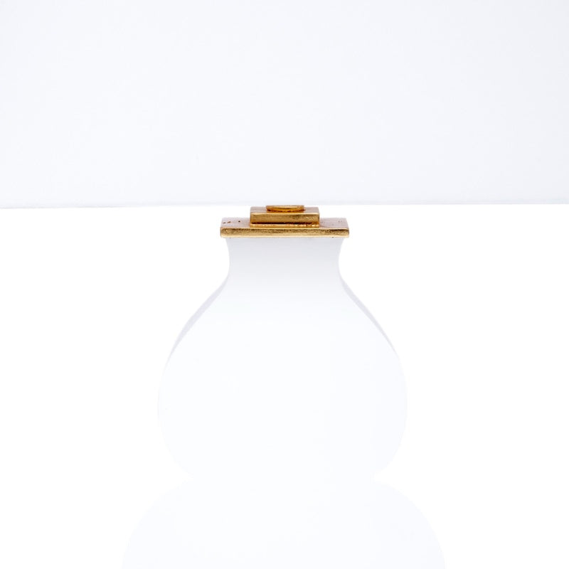 Table lamp with white fabric shade and white glass body, featuring gold accents at top and base