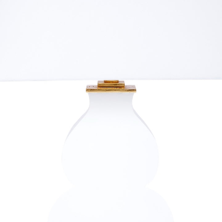 Table lamp with white fabric shade and white glass body, featuring gold accents at top and base