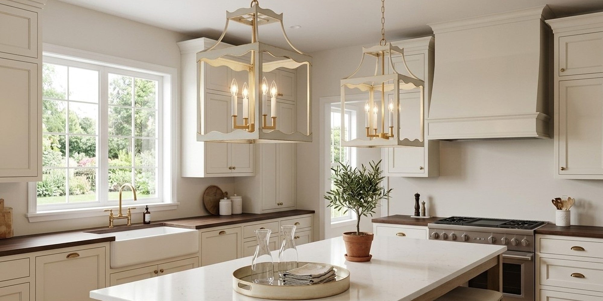 A bright, modern kitchen featuring two ornate gold and cream pendant lights hanging over a white island, surrounded by cream cabinetry, dark wood countertops, and a large window.