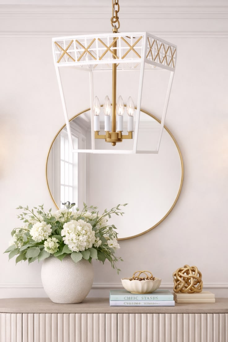 Decorative mirror with gold frame, hanging chandelier, and floral arrangement on a console table.