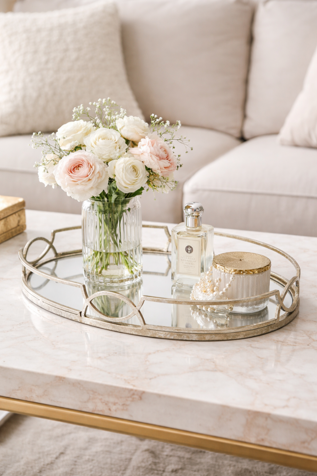 Decorative tray with flowers, candles, and a bottle on a marble coffee table.