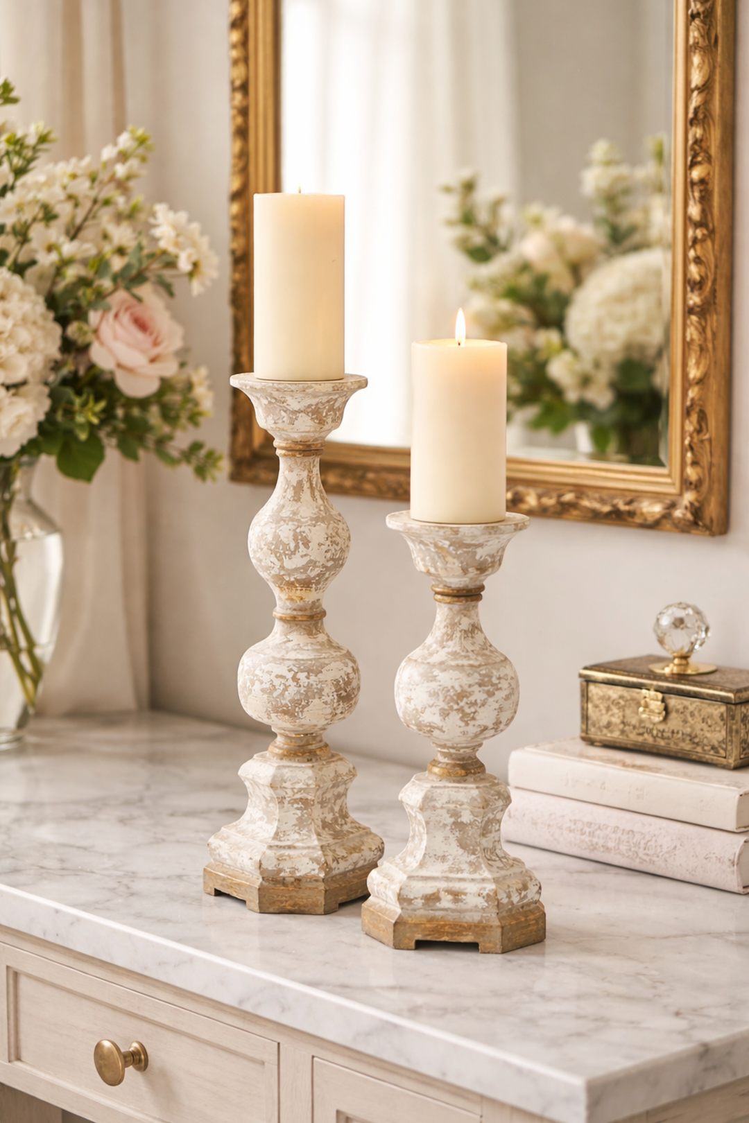 Decorative candle holders on a marble surface with a mirror and flowers in the background