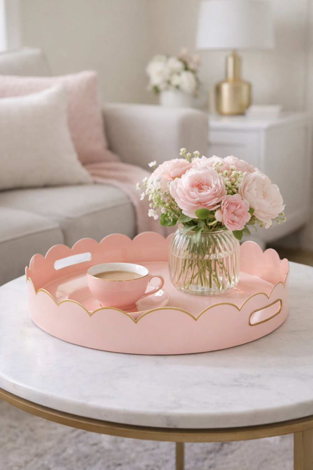 Pink decorative tray with a cup and vase of flowers on a marble table in a living room.