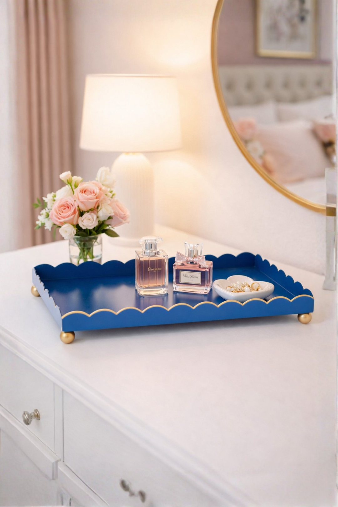 Blue decorative tray with a lamp, flowers, and perfume bottles on a dresser.