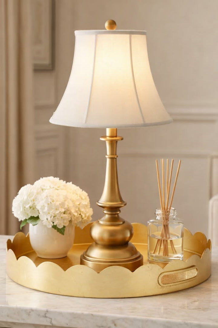 Gold lamp with white shade on a decorative tray with flowers and diffuser