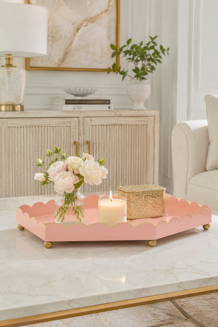 Pink scalloped metal tray with gold rim, holding candles on gold feet