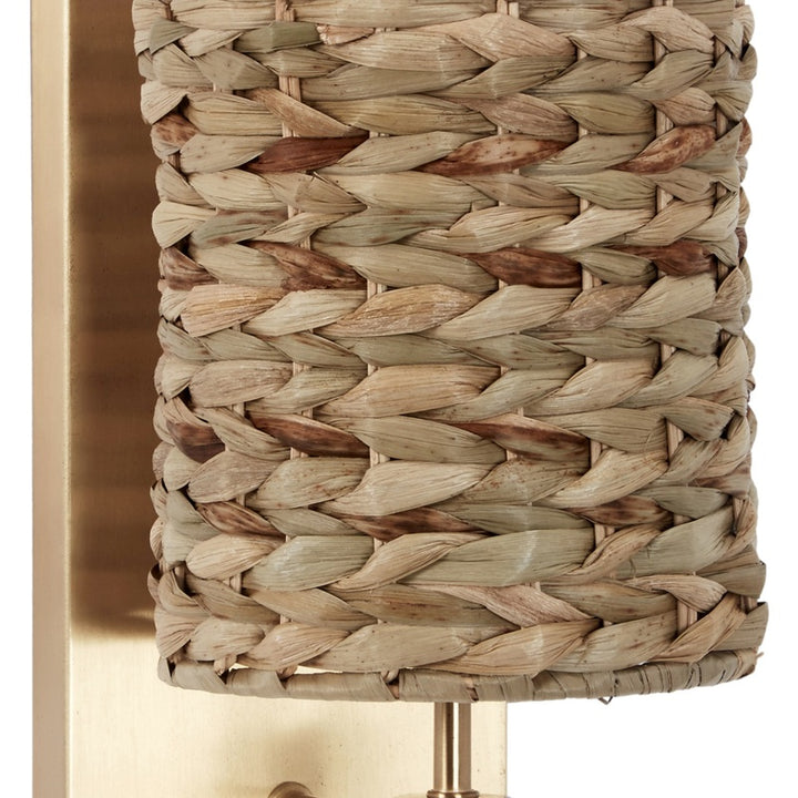 Gold wall sconce with woven water hyacinth shade and brass-toned mounting stem